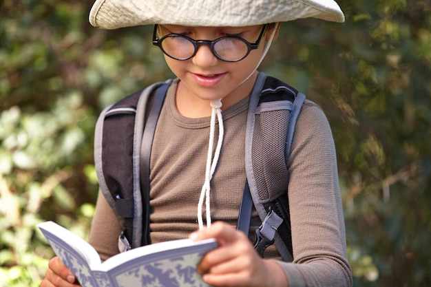 Zdjęcie szczęśliwy mały chłopiec i książka do czytania w lesie dla przewodnika podróży przygody lub odkrycia na świeżym powietrzu mężczyzna dziecko lub dziecko z okularami kapelusz i notatnik do eksploracji historii lub badań w przyrodzie