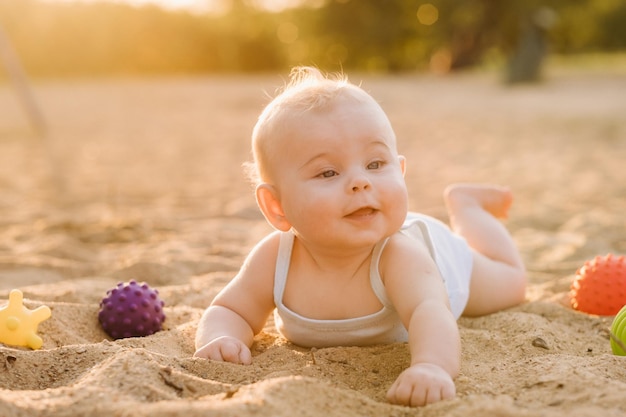 Szczęśliwy mały chłopiec leży na piaszczystej plaży w pobliżu morza w promieniach zachodzącego słońca