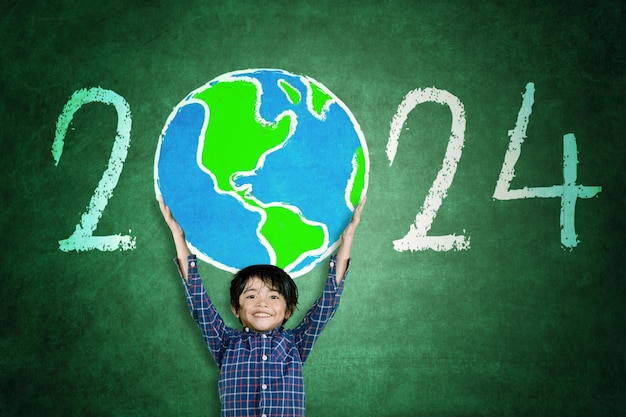 Zdjęcie szczęśliwy mały chłopiec podnoszący kulę ziemską narysowaną numerami nowego roku 2024