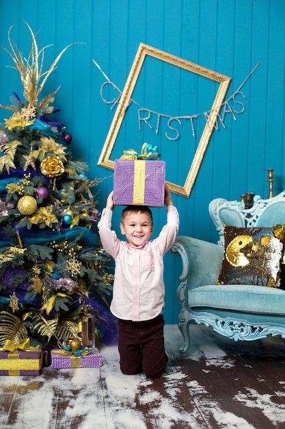 Szczęśliwy mały chłopiec uśmiechający się trzyma pudełko świąteczne.