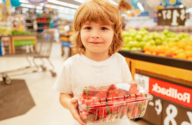 Szczęśliwy mały klient chłopiec z truskawkami zakupy w sklepie spożywczym supermarket chłopiec robi zakupy w