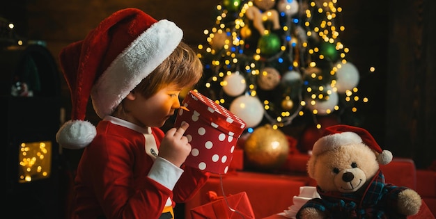 Szczęśliwy mały uśmiechnięty chłopiec z pudełkiem prezentów świątecznych zaskoczył dziecko otwierające prezent świąteczny