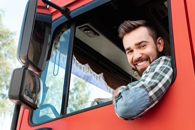 Szczęśliwy męski kierowca ciężarówki w swojej czerwonej ciężarówce