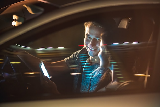 Szczęśliwy mężczyzna i kobieta siedzi w samochodzie i telefonie. wieczorna pora nocna