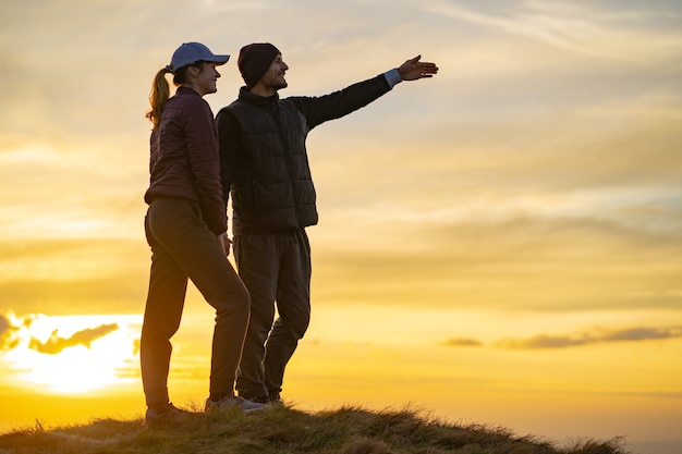 Szczęśliwy mężczyzna i kobieta stojący na wzgórzu na tle zachodu słońca