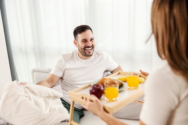 Szczęśliwy mężczyzna je śniadanie w łóżku przyniesione przez żonę w ich przytulnym domu
