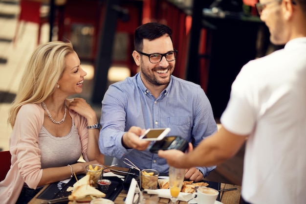 Szczęśliwy Mężczyzna Jedzący Lunch Ze Swoją Dziewczyną W Barze I Płacący Rachunek Smartfonem