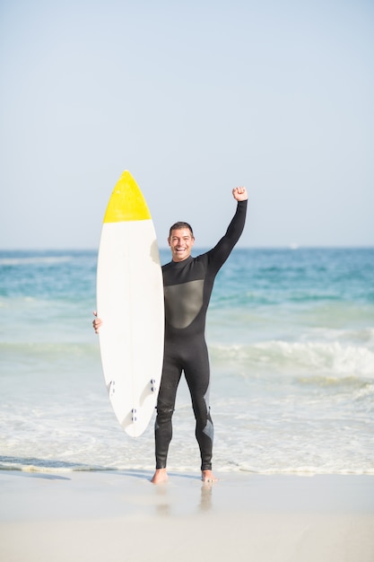 Szczęśliwy mężczyzna trzyma surfboard na plaży