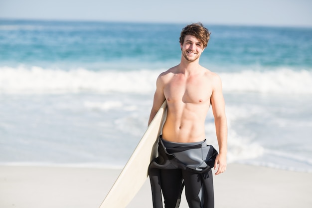 Szczęśliwy mężczyzna trzyma surfboard na plaży