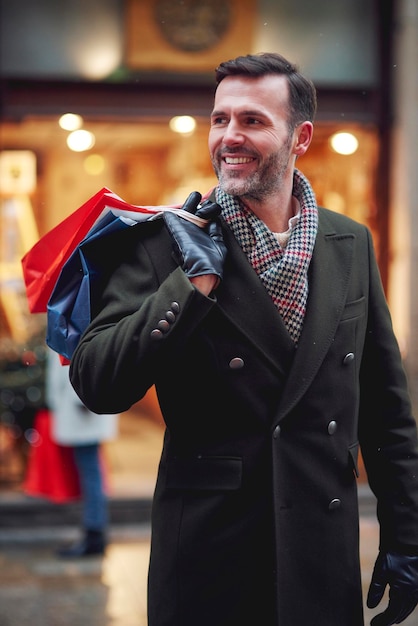 Zdjęcie szczęśliwy mężczyzna trzymający torby na zakupy, stojąc w mieście w zimie