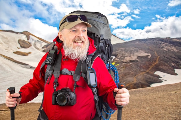 Szczęśliwy mężczyzna z brodą podróżuje z sprzętem turystycznym na tle góry