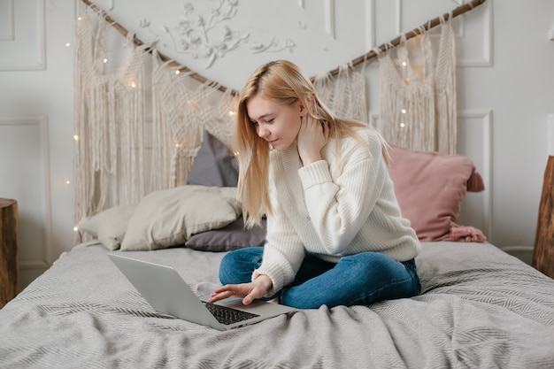Szczęśliwy młodej kobiety spojrzenie przy laptopem siedzi na łóżku w domu