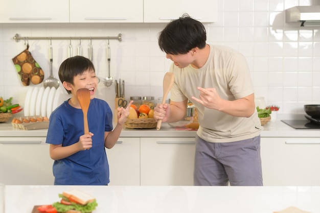 Szczęśliwy młody azjatycki ojciec i syn robią śniadanie razem figlarnie w kuchni w domu