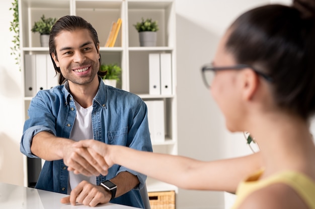 Zdjęcie szczęśliwy młody biznesmen sukcesu uścisk dłoni nowego partnera biznesowego po zawarciu transakcji, patrząc na nią z uśmiechem