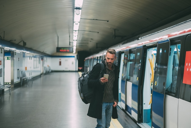 Szczęśliwy młody blondynka mężczyzna z plecakiem wśrodku staci metru czeka pociąg