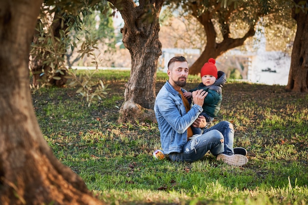 Szczęśliwy młody brodaty mężczyzna bawić się z jego małym synem w parku