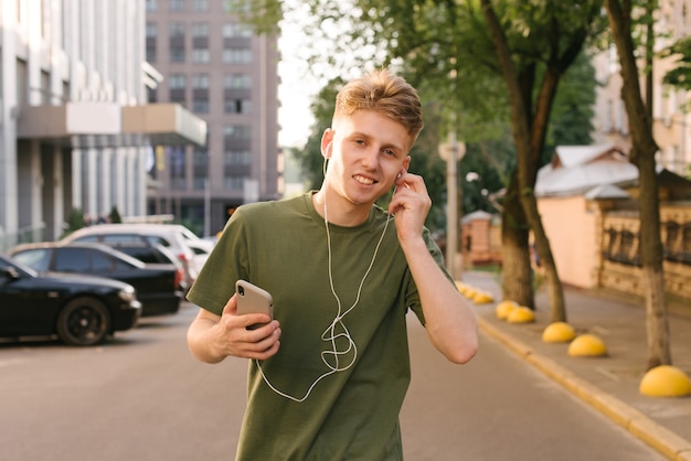 Szczęśliwy młody chłopak w zielonej koszulce spacerując po mieście ze smartfonem w rękach