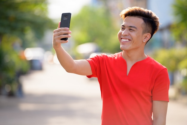 Szczęśliwy młody człowiek Azji biorąc selfie na ulicach na zewnątrz