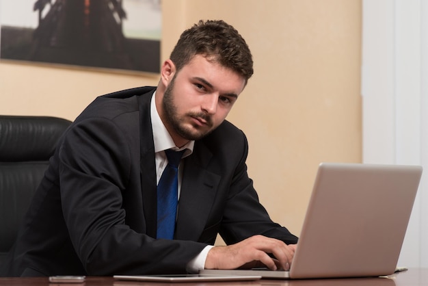 Szczęśliwy młody człowiek biznesu pracuje w nowoczesnym biurze na komputerze