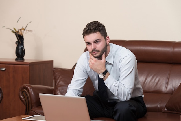Szczęśliwy młody człowiek biznesu pracuje w nowoczesnym biurze na komputerze