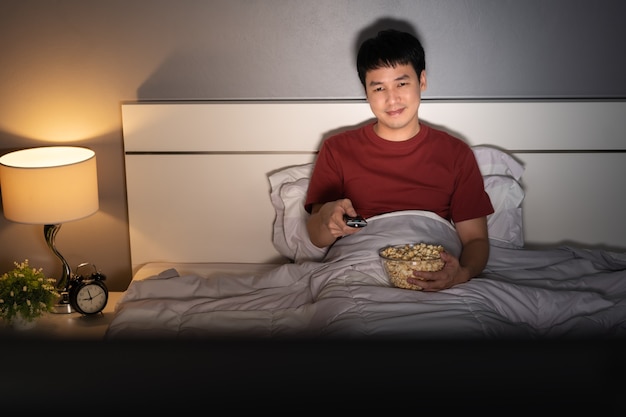 Szczęśliwy młody człowiek ogląda telewizję na łóżku w nocy