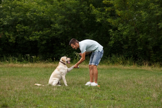 Zdjęcie szczęśliwy młody człowiek trenuje psa labrador na zewnątrz