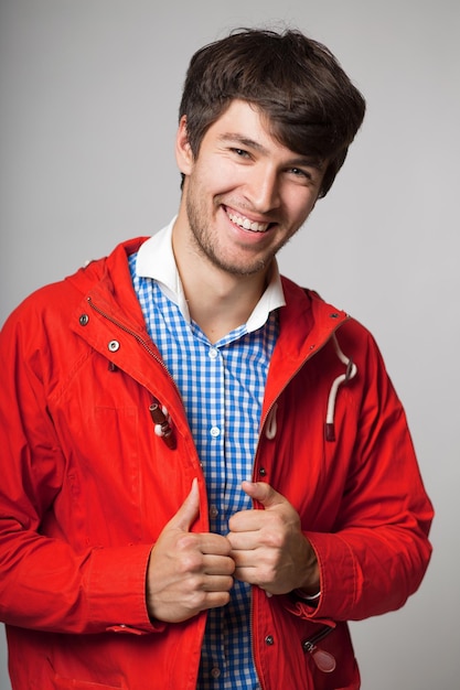 szczęśliwy młody człowiek uśmiechający się w niebieskiej koszuli w kratę i czerwonej kurtce