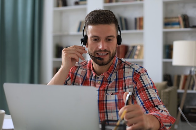 Szczęśliwy młody człowiek w słuchawkach pracuje na laptopie z domu podczas samoizolacji.