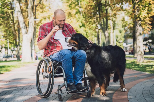 Szczęśliwy młody człowiek z niepełnosprawnością fizyczną na wózku inwalidzkim ze swoim psem