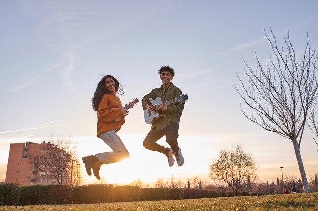 Szczęśliwy młody mężczyzna i młoda kobieta skaczą z gitarą i ukulele przez błękitne niebo