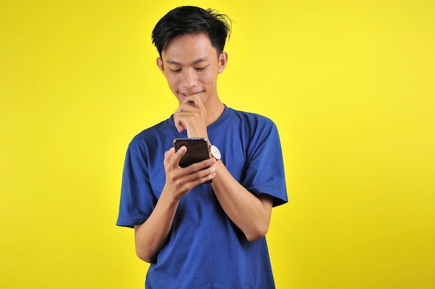 Szczęśliwy młody przystojny Azjata uśmiechający się za pomocą smartfona na żółtym tle