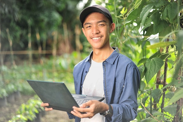 Szczęśliwy młody rolnik z Azji uśmiechający się podczas sprawdzania jakości długiej fasoli za pomocą laptopa