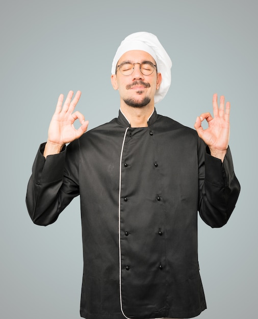 Szczęśliwy młody szef kuchni robi gestowi medytacja