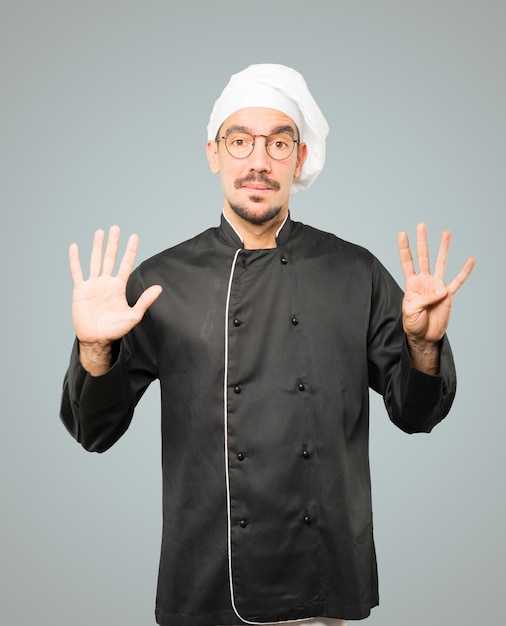 Szczęśliwy młody szef kuchni robi numerowi dziewięć gestowi z jego rękami