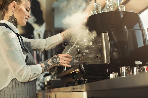 Szczęśliwy młody wytatuowany barista robi kawę w profesjonalnym ekspresie do kawy. Kobieta przygotowuje napój. Koncepcja parzenia kawy dla małych firm i profesjonalnych