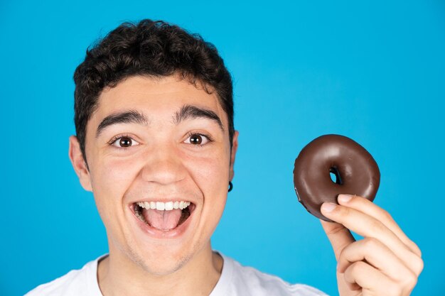 Szczęśliwy nastolatek latynoski chłopiec trzyma czekoladowego pączka lub pączka i uśmiecha się do kamery