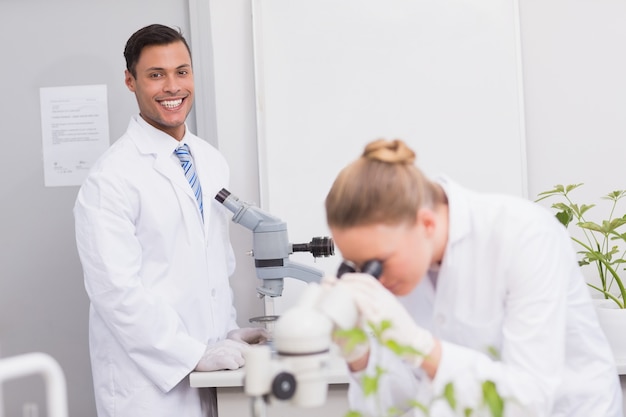 Szczęśliwy naukowiec ono uśmiecha się przy kamerą używać mikroskop w laboratorium