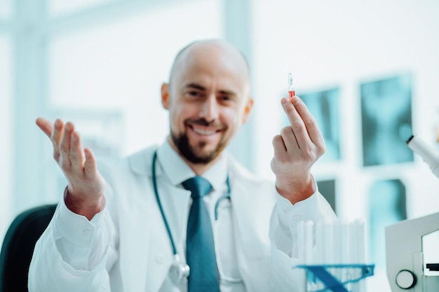 Szczęśliwy naukowiec siedzący przy stole laboratoryjnym z ampułką szczepionki