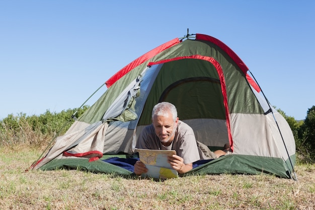Szczęśliwy obozowicz patrzeje mapy lying on the beach w jego namiocie