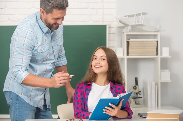 Szczęśliwy ojciec i dziecko uczą się w szkole z książką na temat edukacji na tablicy