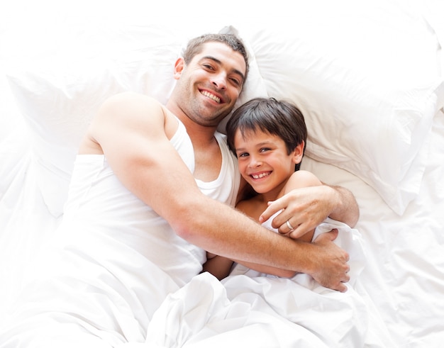 Szczęśliwy ojciec i jego syn patrzeje kamerę na łóżku