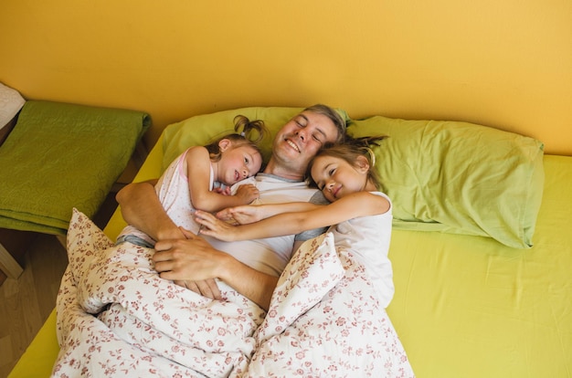 Szczęśliwy ojciec leży w łóżku z dwiema małymi córkami. wypoczynek i relaks