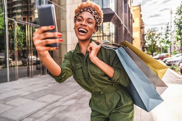 Szczęśliwy Piękny Afro American Kobieta Spacerując Trzymając Torby Na Zakupy I Biorąc Selfie Na Telefon