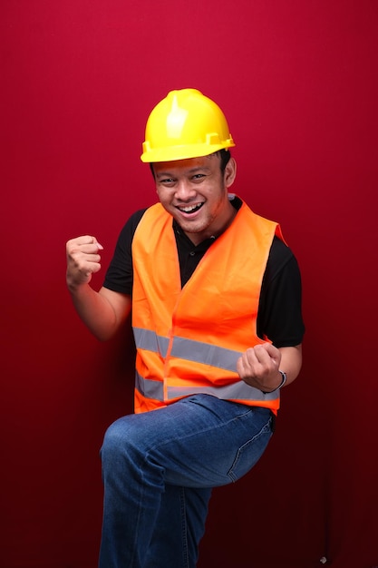 Szczęśliwy, podekscytowany i uśmiechnięty młody pracownik z Azji, podnoszący rękę, by uczcić sukces lub osiągnięcie
