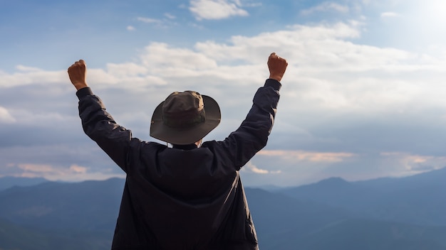 Szczęśliwy podróżnik człowiek stojący i podnieś ręce, aby pokazać sukces na szczycie góry