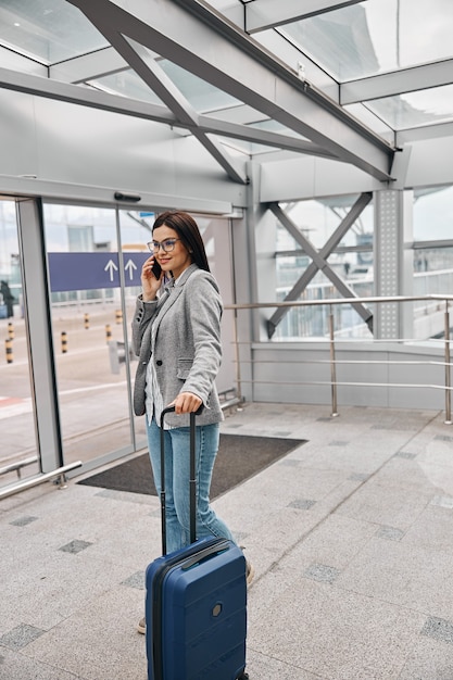 Szczęśliwy podróżnik kaukaski kobieta w terminalu lotniska z bagażem