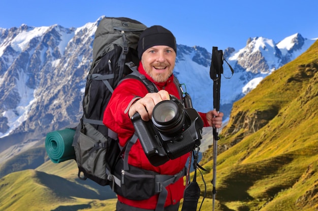 Szczęśliwy podróżnik z aparatem i kijkami trekkingowymi w dłoniach na tle gór