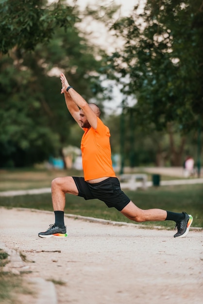 Szczęśliwy pozytywny sportowiec podczas treningu na świeżym powietrzu mężczyzna ubrany w strój sportowy rozgrzewający mięśnie cieszący się aktywnym stylem życia na zewnątrz w parku