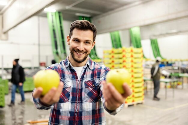 Szczęśliwy pracownik fabryki owoców oferujący jabłka stojąc w magazynie