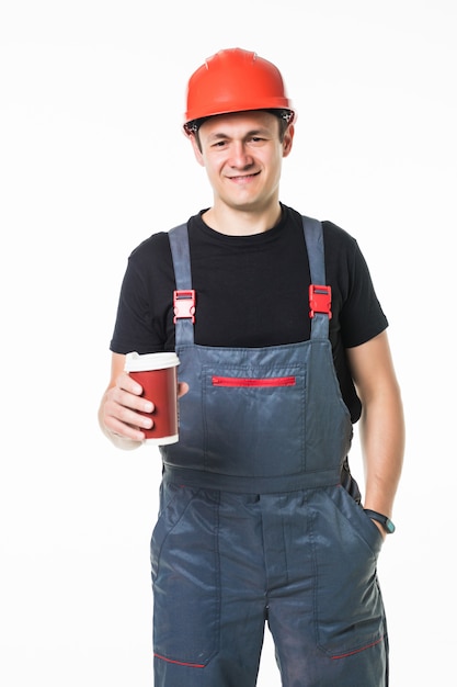 Szczęśliwy pracownik trzyma papierową filiżankę z kawą iść w twardym kapeluszu i ono uśmiecha się przy kamerą